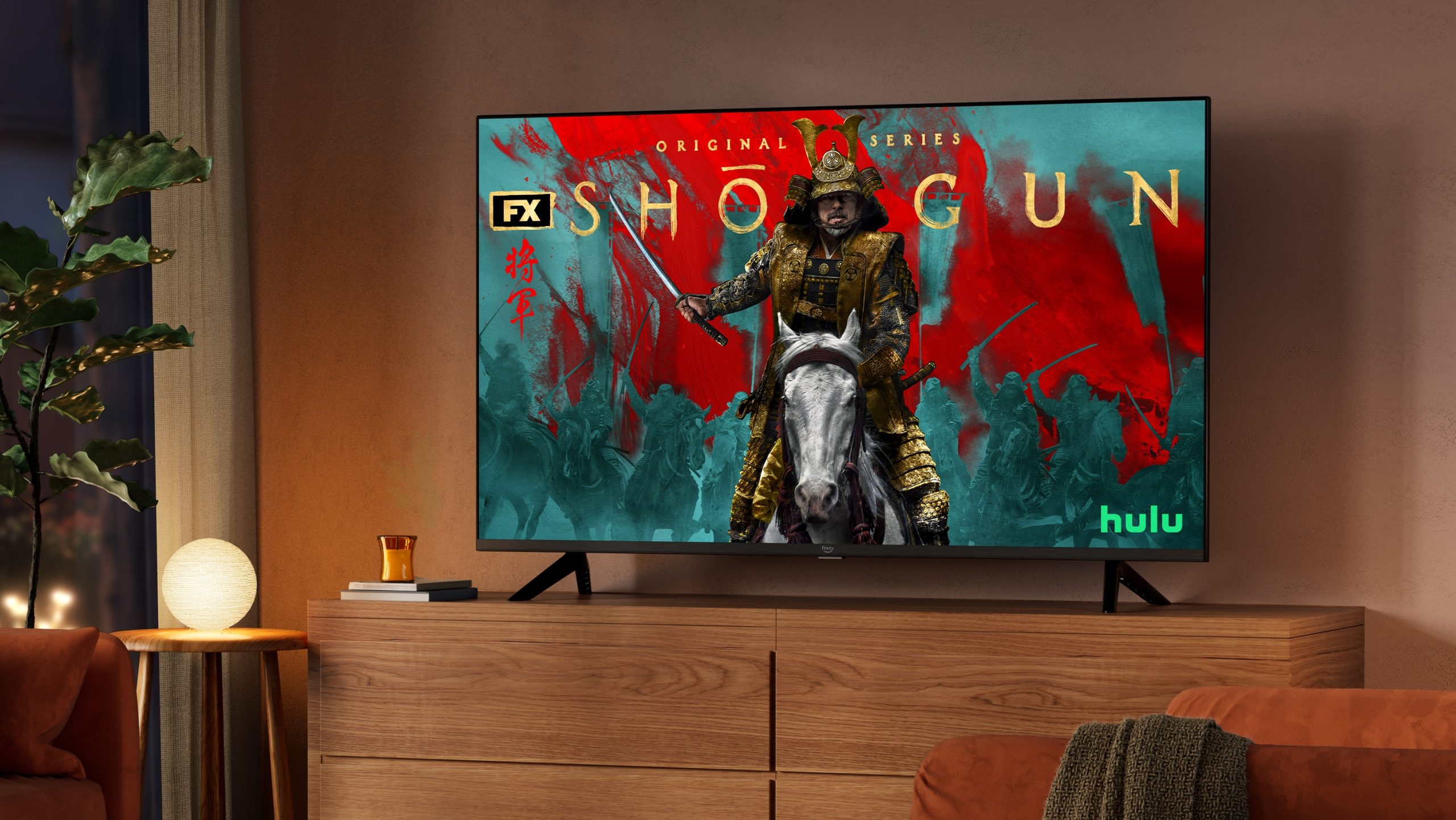 A dimly lit living room in the evening. The Fire TV 4-Series sits on an entertainment center, with Shogun from Hulu on screen. 